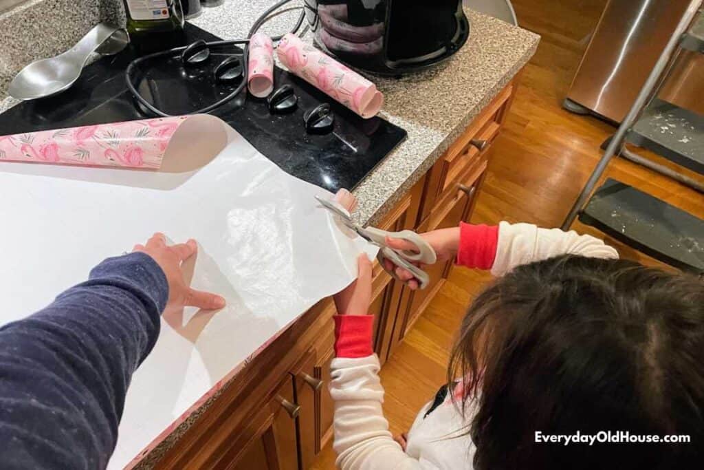 child cutting wrapping paper to go up to kitchen cupboard