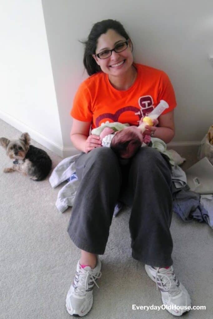 woman sitting on floor during moving day feeding baby her bottle with dog nearby relaxing
