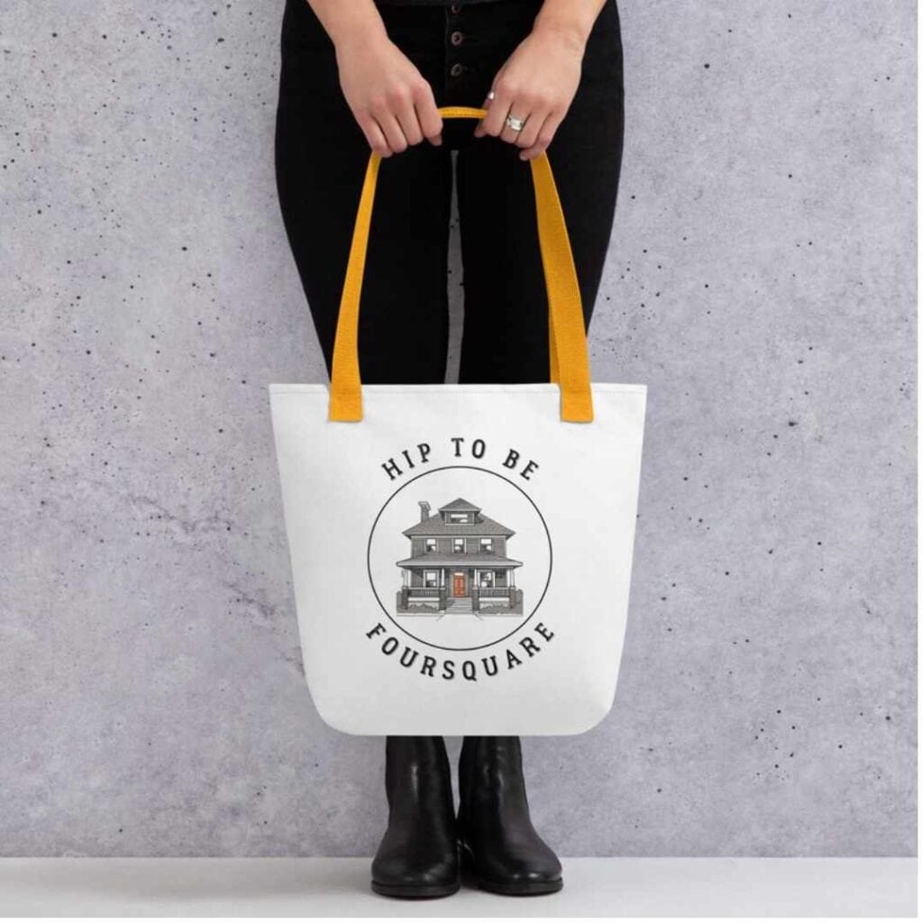 gift idea - woman holding a white tote back with burnt orange straps with a pencil drawing of a American Foursquare house with a title "Hip to be Foursquare"