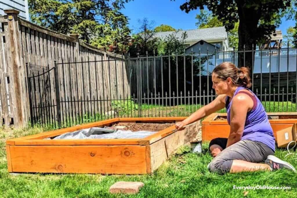 woman sitting on grass staining and resealing wood on raised vegetable garden bed